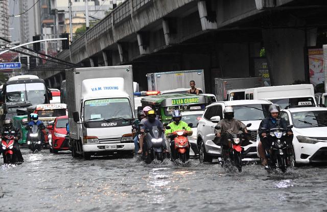 Motorists commute along a flooded street triggered by heavy monsoon rains in Manila on Augsut 17, 2026. (Photo by Ted ALJIBE / AFP)