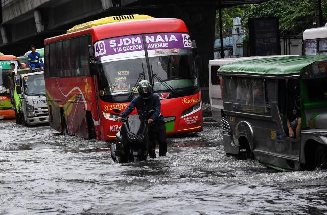 Motorists commute along a flooded street triggered by heavy monsoon rains in Manila on Augsut 17, 2026. (Photo by Ted ALJIBE / AFP)