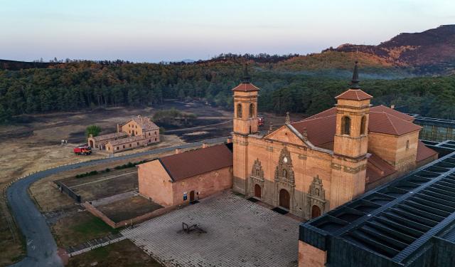 An aerial picture taken early on August 17, 2026 shows a view of the San Juan de la Pena Monastery in Penas de Riglos and burnt land as firefighters (L) are on guard to protect it from a wildfire, in the Spanish northeastern province of Aragon amid a wildfire that burnt 16,600 hectares. A Spanish soldier died on August 16, 2026 while helping efforts to extinguish a major wildfire in the northeastern region of Aragon. The fire that has raged for a week threatened a 1,000-year-old monastery, sheltering the bones of the first Aragonese kings, founders of the Kingdom of Aragon. (Photo by Oscar DEL POZO / AFP)