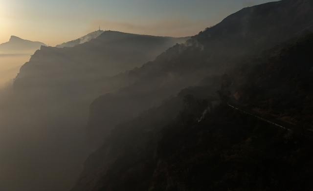 An aerial picture taken early on August 17, 2026 shows smoke and fog on the mountainsides near the San Juan de la Pena Monastery in Penas de Riglos in the Spanish northeastern province of Aragon amid a wildfire that burnt 16,600 hectares. A Spanish soldier died on August 16, 2026 while helping efforts to extinguish a major wildfire in the northeastern region of Aragon. The fire that has raged for a week threatened a 1,000-year-old monastery, sheltering the bones of the first Aragonese kings, founders of the Kingdom of Aragon. (Photo by Oscar DEL POZO / AFP)