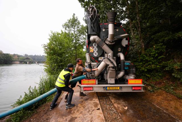 People fills up his water tank in a Luxembourgian truck near the dam of Robertville's lake in Waimes, eastern Belgium on August 17, 2026, during a wildfire burning in the Hautes Fagnes (High Fens) nature reserve. Rain started falling in Belgium on August 17, 2026 to help its fight against the country's biggest modern-day wildfire that has devastated some 3,000 hectares (7,500 acres) of the High Fens park on the border with Germany. Some 500 firefighters and troops are battling the blaze that has sent a huge cloud of black smoke across the region into neighbouring Germany and France. (Photo by JOHN THYS / AFP)