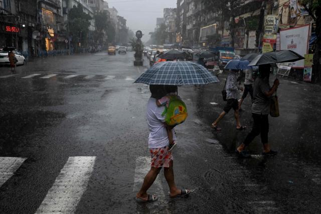 People carrying umbrellas cross a street during rainfall in Kolkata on August 17, 2026. (Photo by Dibyangshu SARKAR / AFP)