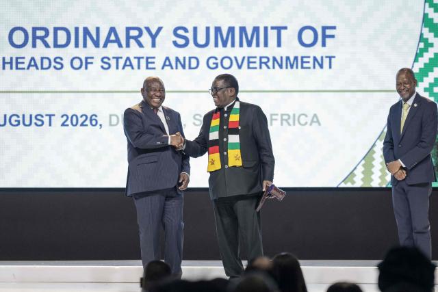Southern African Development Community (SADC) Executive Secretary Elias Magosi (R) reacts as South Africa's President and outgoing SADC chairperson Cyril Ramaphosa (L) shake hands with Zimbabwe's President Emmerson Mnangagwa (R) after the handover of the rotating leadership during the 46th Southern African Development Community (SADC) Summit at the Durban International Convention Centre (ICC), in Durban on August 17, 2026. (Photo by Rajesh JANTILAL / AFP)