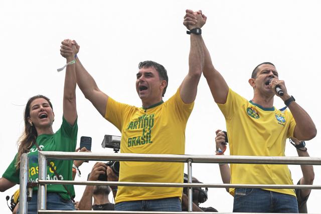 Brazil’s right-wing presidential candidate and senator Flavio Bolsonaro (C), his wife Fernanda Bolsonaro (L), and Rio de Janeiro’s candidate for Governor and congressman Douglas Ruas (R), gesture to supporters during a campaign rally at Copacabana Beach in Rio de Janeiro, Brazil, on August 16, 2026. Brazilians will go to the polls next October 4 once again deeply polarized and under the shadow of US President Donald Trump, who has backed conservative candidates in recent elections in Latin America. (Photo by MAURO PIMENTEL / AFP)