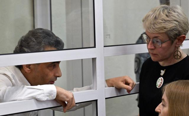 A bailiff puts handcuffs on Russian opposition politician Lev Shlosberg, who has been sentenced to 11 years in prison over his criticism of Moscow's offensive in Ukraine, talks to his wife Zhanna Shlosberg-Kozlovich at a city court in Pskov, northwestern Russia on August 17, 2026. The veteran Yabloko party member was found guilty of "public actions aimed at discrediting the use of the Armed Forces of the Russian Federation". (Photo by Olga MALTSEVA / AFP)