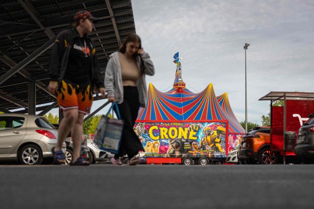 Shoppers walk in the car park of a Carrefour Market where the Crone Circus Big Top is set up in Pont-Audemer, on August 17, 2026. Traveling circus' have been marked by some recurring tensions regarding unauthorized installations on public or private land. (Photo by JOEL SAGET / AFP)