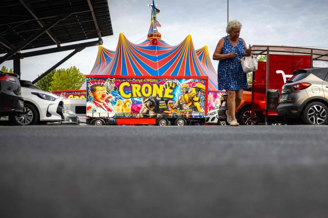 Shoppers walk in the car park of a Carrefour Market where the Crone Circus Big Top is set up in Pont-Audemer, on August 17, 2026. Traveling circus' have been marked by some recurring tensions regarding unauthorized installations on public or private land. (Photo by JOEL SAGET / AFP)