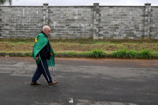 A man wrapped in a Brazilian flag walks outside Francisco Alvares de Assis Airport in Juiz de Fora, Minas Gerais state, Brazil, on August 17, 2026, after organizers cancelled presidential candidate Flavio Bolsonaro's event due to weather conditions. (Photo by Pablo PORCIUNCULA / AFP)