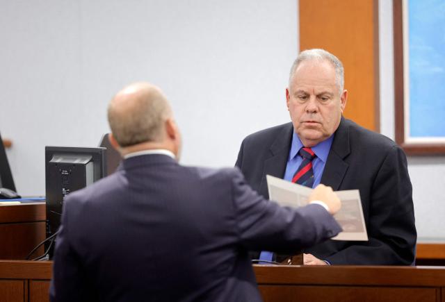 Chief Deputy District Attorney Marc DiGiacomo (L) shows a photo to Garry Dale, a former Las Vegas Metro Police Department officer, during the Duane Davis murder trial, related to the 1996 killing of rapper Tupac Shakur, at Clark County District Court Regional Justice Center in Las Vegas,  Nevada, on August 17, 2026. The trial of the former gang leader accused of orchestrating the murder of rapper Tupac Shakur began on August 10, 30 years after one of America's most high-profile unresolved killings. The proceedings, expected to last a month, will likely not make clear who fired the shots that killed the California hip-hop legend on the night of September 7, 1996, while he was in Las Vegas to see a Mike Tyson boxing match. (Photo by STEVE MARCUS / POOL / AFP)