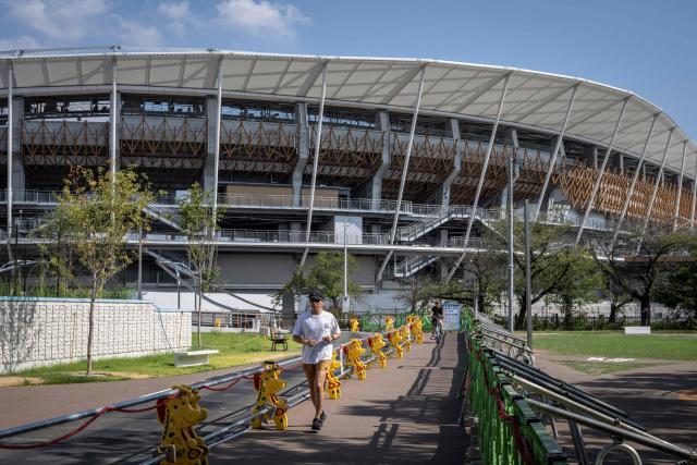 (FILES) This picture taken on September 7, 2025 shows a man jogging past the Nagoya City Mizuho Park Athletic Stadium, the venue for track and field and marathon competitions at the 2026 Asian Games, which is currently under construction in Nagoya, Aichi prefecture. The Asian Games begin in Japan on September 19, 2026 featuring teenage prodigies, more athletes than the Olympics and a cruise ship that will house competitors in the middle of typhoon season. (Photo by Yuichi YAMAZAKI / AFP)