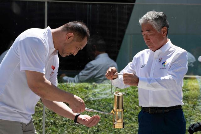 Japanese former hammer throw athlete Koji Murofushi (L) and Vice President of the Olympic Council of Asia Tsunekazu Takeda take part in the torch lighting ceremony for the 2026 Asian Games, outside the National Stadium in Tokyo on August 18, 2026. About 15,000 competitors and officials are expected at the event, which takes place in Nagoya and the wider Aichi area from September 19 to October 4. (Photo by Yuichi YAMAZAKI / AFP)