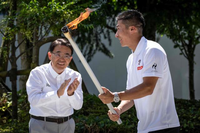 Japanese sprinter Yoshihide Kiryu (R) and Governor of Aichi Prefecture Hideaki Omura take part in the torch lighting ceremony for the 2026 Asian Games, outside the National Stadium in Tokyo on August 18, 2026. About 15,000 competitors and officials are expected at the event, which takes place in Nagoya and the wider Aichi area from September 19 to October 4. (Photo by Yuichi YAMAZAKI / AFP)