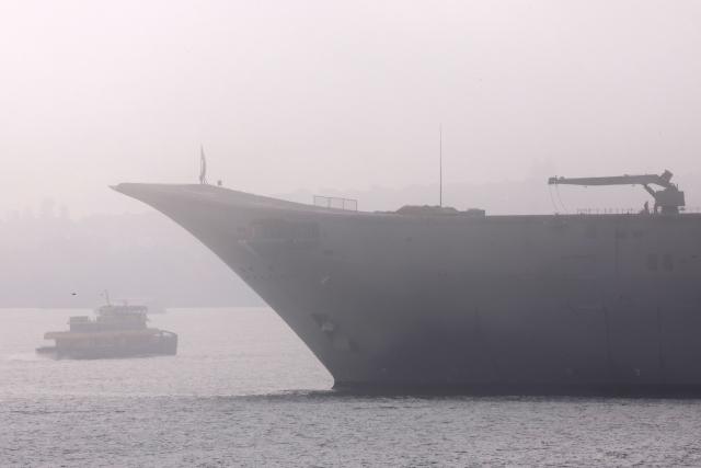 A ferry sails on a foggy morning past an old aircraft carrier docked at a naval base located on Sydney Harbour in Sydney on August 18, 2026. (Photo by DAVID GRAY / AFP)