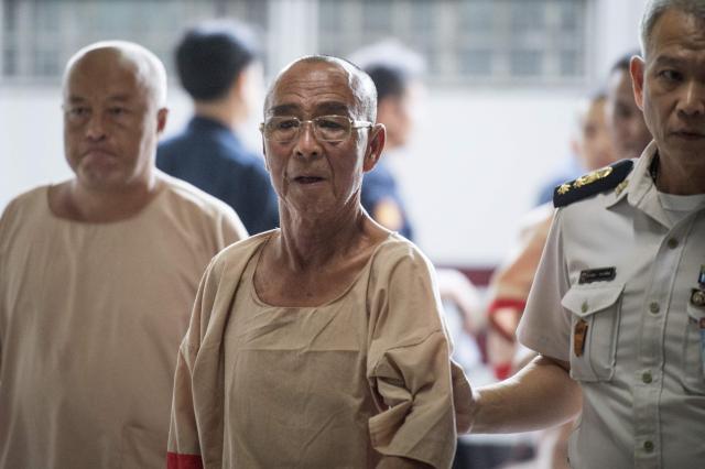 (FILES) Laota Seanlee (C), a controversial guerilla fighter long accused of playing a key role in the Golden Triangle drugs trade, is escorted into a Criminal Court in Bangkok on December 13, 2017. Thailand's justice minister pledged on August 18, 2026 to review pardon criteria following backlash over the release of 85-year-old drug trafficker Laota Saenlee who served less than a decade of a life prison sentence. (Photo by LILLIAN SUWANRUMPHA / AFP)