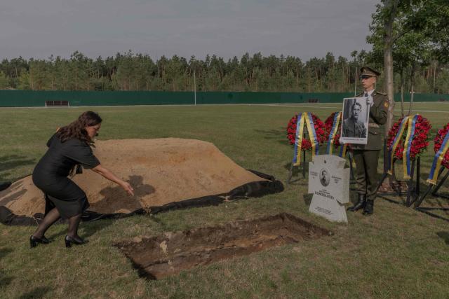 A woman tosses handfuls of soil over the coffin bearing the repatriated remains of Yevhen Konovalets, leader of the Organisation of Ukrainian Nationalists (OUN), who was killed by a Soviet agent in 1938, during his reburial ceremony at the National Military Memorial Cemetery near Kyiv on August 18, 2026, amid the Russian invasion of Ukraine. (Photo by Roman PILIPEY / AFP)