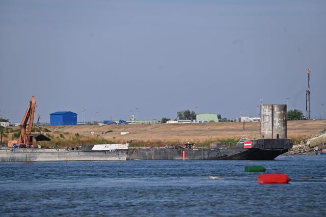 The controlled sinking of two 80-meter-long barges loaded with rocks is under way on the section of the Danube adjacent to the Paks Nuclear power Plant near Dunaszentbenedek, Hungary, on August 18, 2026. Hungary has so far been able to avoid a complete shutdown of its only nuclear plant, Paks, whose four reactors are cooled by the Danube. But the Hungarian government has ordered the construction of a submerged wall, or weir, to try to control flows nears the plant. Two 80-metre barges are sunk to raise the water level. Paks, whose output usually covers around a third of Hungary's electricity needs, has been partially shut down since July 2026 due to a drought scorching Europe that has caused the Danube river to fall to record lows. (Photo by Attila KISBENEDEK / AFP)