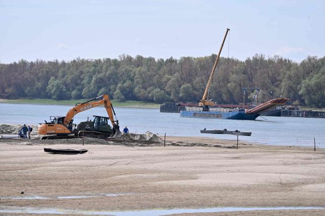 The controlled sinking of two 80-meter-long barges (background) loaded with rocks is under way on the banks of the river Danube on the section of the Danube adjacent to the Paks nuclear power plant near Dunaszentbenedek, Hungary, on August 18, 2026. Hungary has so far been able to avoid a complete shutdown of its only nuclear plant, Paks, whose four reactors are cooled by the Danube. But the Hungarian government has ordered the construction of a submerged wall, or weir, to try to control flows nears the plant. Two 80-metre barges are sunk to raise the water level. Paks, whose output usually covers around a third of Hungary's electricity needs, has been partially shut down since July 2026 due to a drought scorching Europe that has caused the Danube river to fall to record lows. (Photo by Attila KISBENEDEK / AFP)