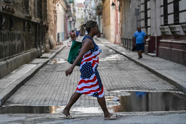 A woman wearing a dress with the US flag crosses a street in Havana on August 18, 2026. Once synonymous with carefree revelry, Havana has been deserted due to power cuts, mass emigration and deep uncertainty about its future. (Photo by YAMIL LAGE / AFP)