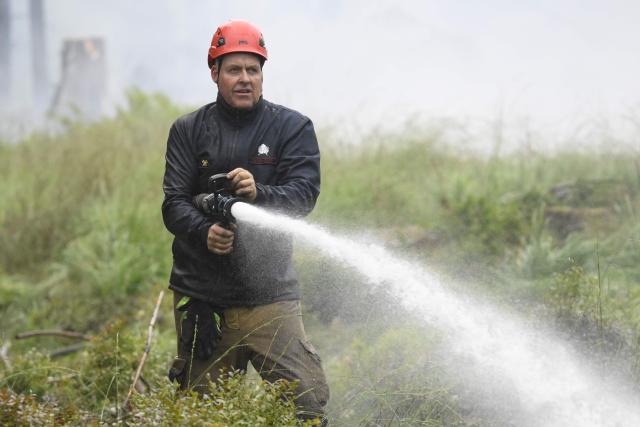 A firefighter sprays water from a hose during operations against a wildfire at the Hautes Fagnes (High Fens) nature reserve near Baelen, on August 18, 2026. Rain started falling in Belgium on August 17, 2026 to help its fight against the country's biggest modern-day wildfire that has devastated some 3,000 hectares (7,500 acres) of the High Fens park on the border with Germany. Some 500 firefighters and troops are battling the blaze that has sent a huge cloud of black smoke across the region into neighbouring Germany and France. Scientists have long warned that climate change caused by human use of fossil fuels will make periods of drought more intense and longer-lasting, creating the ideal conditions for wildfires. (Photo by JOHN THYS / AFP)