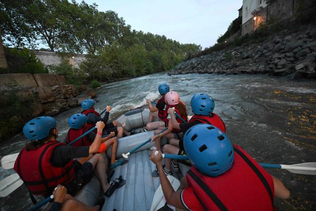 People raft in a rubber dinghy on the Tiber River past Tiberina Island, in a stretch of the river that runs entirely within the urban area of central Rome, on August 14, 2026. Rafting on the Tiber offers relief from Rome heatwave on a rafting route on the Tiber taking place entirely within the urban area and taking approximately two hours. (Photo by Andreas SOLARO / AFP)