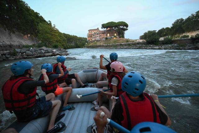 People raft in a rubber dinghy on the Tiber River past Tiberina Island, in a stretch of the river that runs entirely within the urban area of central Rome, on August 14, 2026. Rafting on the Tiber offers relief from Rome heatwave on a rafting route on the Tiber taking place entirely within the urban area and taking approximately two hours. (Photo by Andreas SOLARO / AFP)