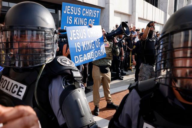 Police in riot gear stand nearby as far-right US activist Jake Lang (C) holds a sign reading "Jesus Christ is King of Dearborn" during an anti-Muslim demonstration he organized called the "Christian Crusade March" in Dearborn, Michigan, on August 18, 2026. (Photo by JEFF KOWALSKY / AFP)