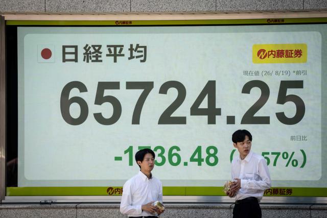 People wait to cross a street in front of an electronic quotation board displaying the Nikkei Stock Average on the Tokyo Stock Exchange in Tokyo on August 19, 2026. (Photo by Yuichi YAMAZAKI / AFP)