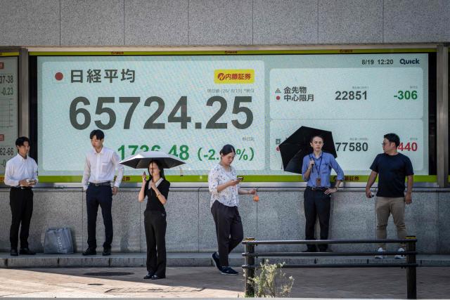 People wait to cross a street in front of an electronic quotation board displaying the Nikkei Stock Average on the Tokyo Stock Exchange in Tokyo on August 19, 2026. (Photo by Yuichi YAMAZAKI / AFP)