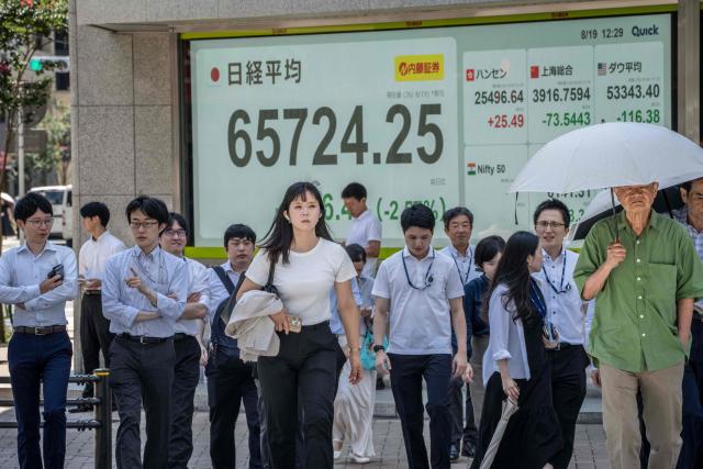 People cross a street in front of an electronic quotation board displaying the Nikkei Stock Average on the Tokyo Stock Exchange in Tokyo on August 19, 2026. (Photo by Yuichi YAMAZAKI / AFP)