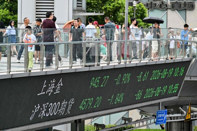 People walk across a footbridge with a screen showing financial market movements at the financial district of Shanghai on August 19, 2026. (Photo by Hector RETAMAL / AFP)