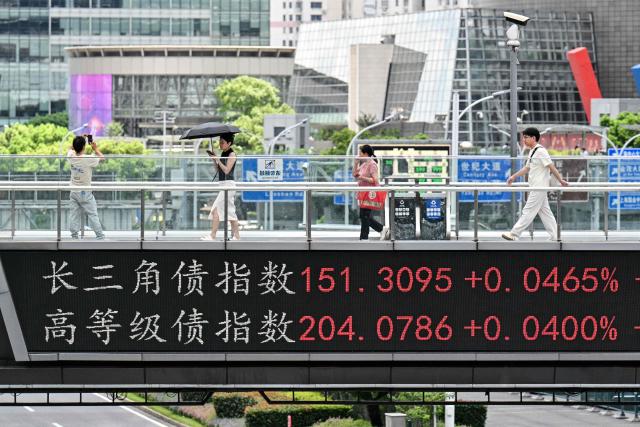People walk across a footbridge with a screen showing financial market movements at the financial district of Shanghai on August 19, 2026. (Photo by Hector RETAMAL / AFP)