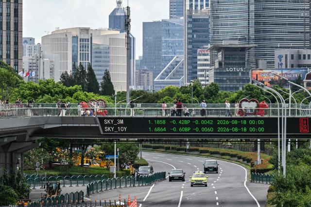 People walk across a footbridge with a screen showing financial market movements at the financial district of Shanghai on August 19, 2026. (Photo by Hector RETAMAL / AFP)
