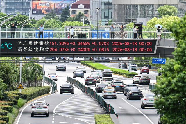 People walk across a footbridge with a screen showing financial market movements at the financial district of Shanghai on August 19, 2026. (Photo by Hector RETAMAL / AFP)