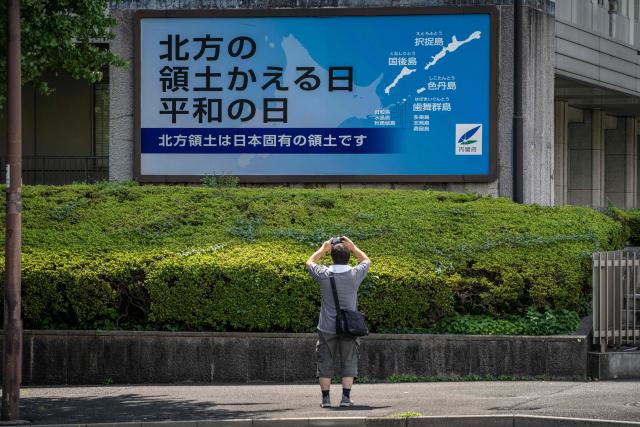 A man takes photographs of a Japanese government sign reading "Day of the Return of the Northern Territories, Day of Peace. The Northern Territories are an inherent part of Japan's territory,"?referring to the Russian-controlled Southern Kuril Islands claimed by Japan as its Northern Territories, in Tokyo on August 19, 2026. Bilateral relations have long been strained over the Kurils, known in Japan as the Northern Territories. After Russia's President Vladimir Putin visited the islands on August 13, Japan summoned the Russian ambassador in protest, and Russia followed suit. (Photo by Yuichi YAMAZAKI / AFP)
