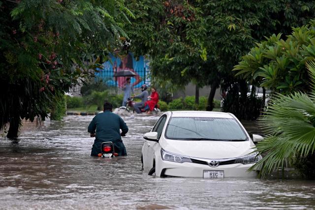 Commuters wade through a flooded street after heavy rainfall in Rawalpindi on August 19, 2026. (Photo by Farooq NAEEM / AFP)