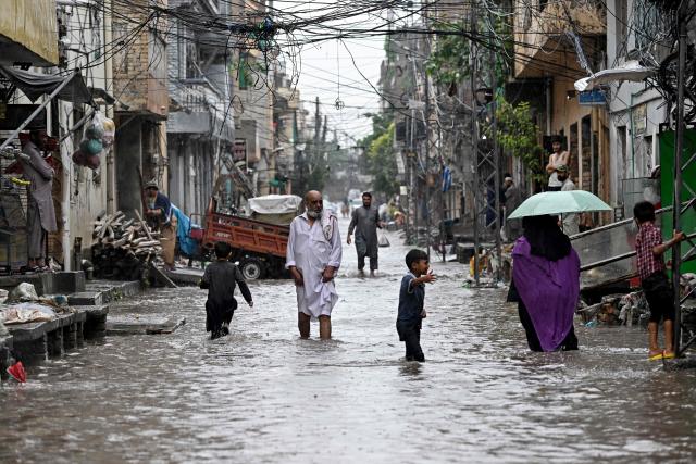 People wade through a flooded street after heavy rainfall in Rawalpindi on August 19, 2026. (Photo by Farooq NAEEM / AFP)