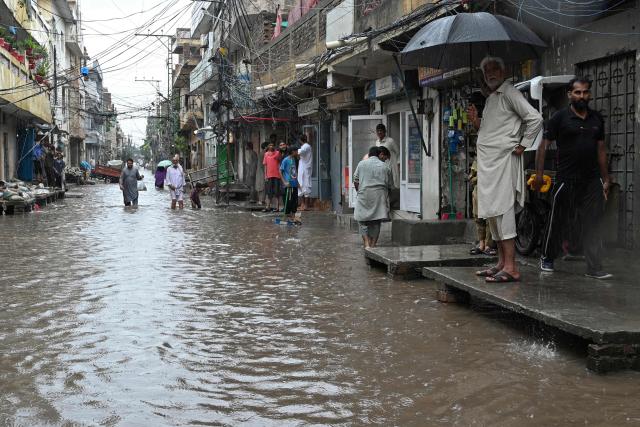 People wade through a flooded street during rainfall in Rawalpindi on August 19, 2026. (Photo by Farooq NAEEM / AFP)
