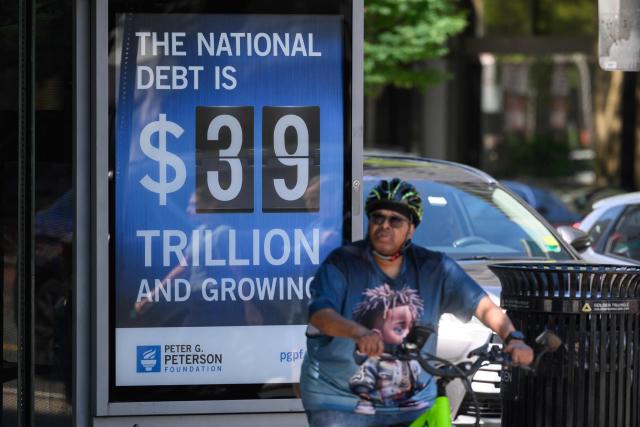 A cyclist pauses in front of a poster showing the US national debt in Washington, DC on August 19, 2026. The US national debt is approaching a record 40 trillion dollars. (Photo by Mandel NGAN / AFP)