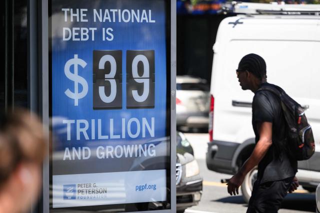 People pass by a poster showing the US national debt in Washington, DC on August 19, 2026. The US national debt is approaching a record 40 trillion dollars. (Photo by Mandel NGAN / AFP)