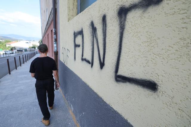 A man walks past nationalist graffiti "FLNC" (Front de liberation nationale de la Corse) on a wall in the town of Corte, in the center of the French Mediterranean island of Corsica, on August 19, 2026. (Photo by Pascal POCHARD-CASABIANCA / AFP)