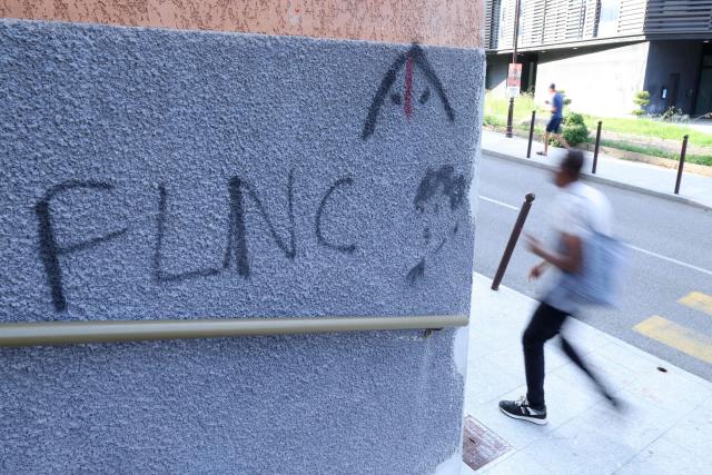 A man walks past nationalist graffiti "FLNC" (Front de liberation nationale de la Corse) on a wall in the town of Corte, in the center of the French Mediterranean island of Corsica, on August 19, 2026. (Photo by Pascal POCHARD-CASABIANCA / AFP)
