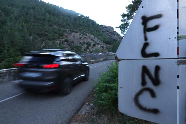 A car drives past a sign with nationalist graffiti "FLNC" (Front de liberation nationale de la Corse) on a wall in the town of Corte, in the center of the French Mediterranean island of Corsica, on August 19, 2026. (Photo by Pascal POCHARD-CASABIANCA / AFP)