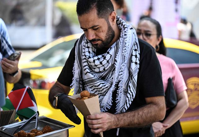 An assistant to Fadi Abed serves falafel to customers at the Palestinian food stall "Hijo de Palestina", in La Plaza del Bolero in Tlalpan, on the outskirts of Mexico City, on August 14, 2026. Abed —one of 18 members of the Abed family, the first refugees to arrive in Mexico following Israeli bombardments of the Gaza Strip— launched a Palestinian food business which went viral and became highly popular thanks to the "Cumbia del Falafel"—a promotional jingle he plays as he drives his tricycle through the streets of Tlalpan and Mexico City. (Photo by Yuri CORTEZ / AFP)