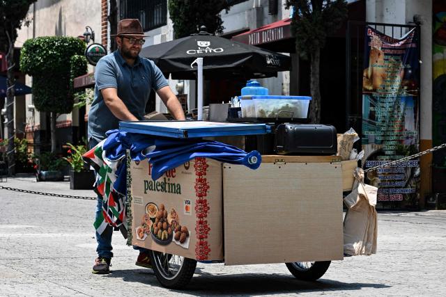Palestinian Fadi Abed pushes his tricycle as he heads to set up his food stall "Hijo de Palestina" in La Plaza del Bolero in Tlalpan, on the outskirts of Mexico City, on August 14, 2026. Abed —one of 18 members of the Abed family, the first refugees to arrive in Mexico following Israeli bombardments of the Gaza Strip— launched a Palestinian food business which went viral and became highly popular thanks to the "Cumbia del Falafel"—a promotional jingle he plays as he drives his tricycle through the streets of Tlalpan and Mexico City. (Photo by Yuri CORTEZ / AFP)