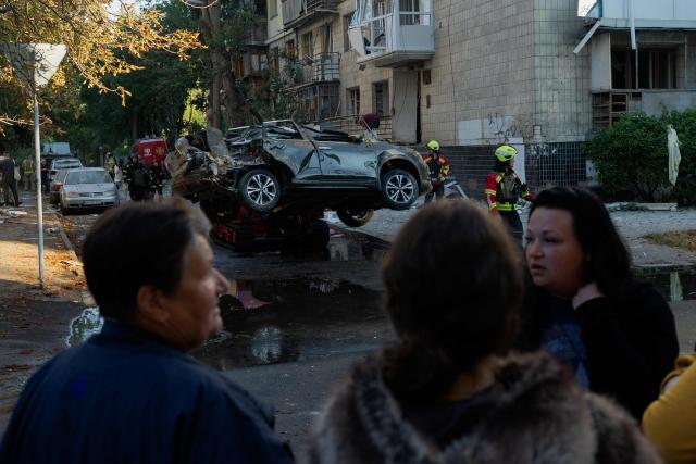 People stand next to a damaged car following a Russian strike in Kyiv on August 20, 2026, amid Russia’s invasion of Ukraine. Russian bombardment killed six people and wounded dozens in Ukraine's capital and its surrounding region overnight, authorities said on August 20. (Photo by Tetiana DZHAFAROVA / AFP)