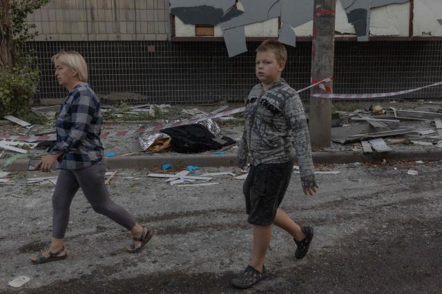 People walk past bodies near a residential building damaged in a Russian strike on Kyiv that also hit a nearby hospital, on August 20, 2026, amid Russia's invasion of Ukraine. Russian bombardments killed at least 12 people and wounded dozens in Ukraine's capital and its surrounding region overnight, authorities said on August 20. (Photo by Roman PILIPEY / AFP)