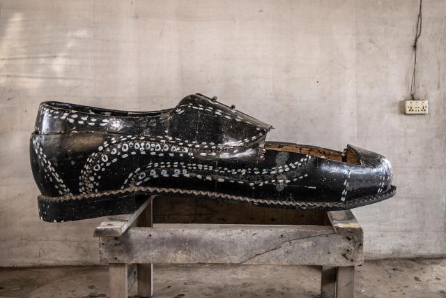 A shoe-shaped coffin, designed in reference to the profession of the deceased, a footballer, is pictured at the Kane Kwei Carpentry Workshop in Accra, on August 17, 2026. Fantasy coffins are a distinctive Ghanaian funerary tradition, particularly associated with the Ga people of the Greater Accra region. Known locally as abebuu adekai (“proverb boxes”), they are handcrafted in the shape of objects, animals or vehicles reflecting the deceased’s profession, personality or interests — from a fish for a fisherman to a shoe for a footballer. Developed around Accra in the mid-20th century, the tradition has evolved into a highly skilled craft. The practice reflects a Ghanaian approach to funerals in which mourning can coexist with celebration, symbolism and a strong emphasis on remembering the life and identity of the deceased. (Photo by OLYMPIA DE MAISMONT / AFP)