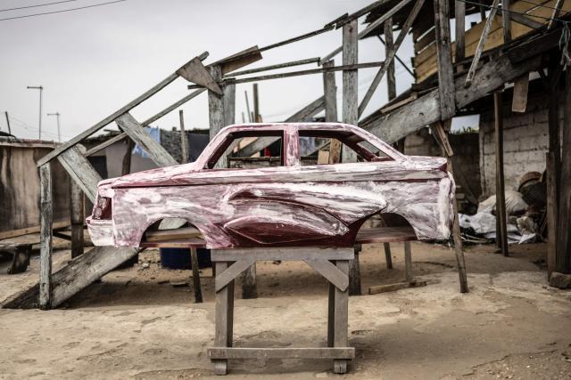 A car-shaped coffin, designed in reference to the profession of the deceased, a driver, is pictured at the Hello Design Coffin workshop in Accra, on August 17, 2026. Fantasy coffins are a distinctive Ghanaian funerary tradition, particularly associated with the Ga people of the Greater Accra region. Known locally as abebuu adekai (“proverb boxes”), they are handcrafted in the shape of objects, animals or vehicles reflecting the deceased’s profession, personality or interests — from a fish for a fisherman to a shoe for a footballer. Developed around Accra in the mid-20th century, the tradition has evolved into a highly skilled craft. The practice reflects a Ghanaian approach to funerals in which mourning can coexist with celebration, symbolism and a strong emphasis on remembering the life and identity of the deceased. (Photo by OLYMPIA DE MAISMONT / AFP)