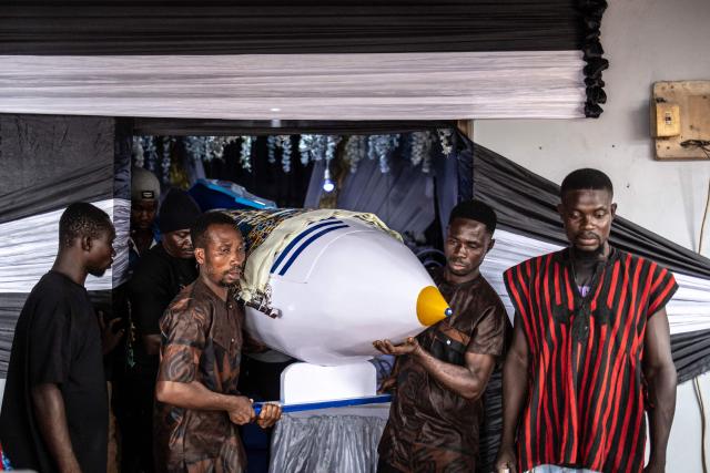 Relatives carry the pen-shaped coffin containing the body of the late Ghanaian teacher Samuel Commey Tetteh following traditional rituals during his funeral ceremony in Paanor, Ghana, on August 15, 2026. Fantasy coffins are a distinctive Ghanaian funerary tradition, particularly associated with the Ga people of the Greater Accra region. Known locally as abebuu adekai (“proverb boxes”), they are handcrafted in the shape of objects, animals or vehicles reflecting the deceased’s profession, personality or interests — from a fish for a fisherman to a shoe for a footballer. Developed around Accra in the mid-20th century, the tradition has evolved into a highly skilled craft. The practice reflects a Ghanaian approach to funerals in which mourning can coexist with celebration, symbolism and a strong emphasis on remembering the life and identity of the deceased. (Photo by OLYMPIA DE MAISMONT / AFP)