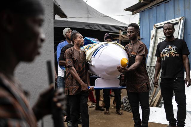 Relatives carry the pen-shaped coffin containing the body of late Ghanaian teacher Samuel Commey Tetteh following traditional rituals during his funeral ceremony in Paanor, Ghana, on August 15, 2026. Fantasy coffins are a distinctive Ghanaian funerary tradition, particularly associated with the Ga people of the Greater Accra region. Known locally as abebuu adekai (“proverb boxes”), they are handcrafted in the shape of objects, animals or vehicles reflecting the deceased’s profession, personality or interests — from a fish for a fisherman to a shoe for a footballer. Developed around Accra in the mid-20th century, the tradition has evolved into a highly skilled craft. The practice reflects a Ghanaian approach to funerals in which mourning can coexist with celebration, symbolism and a strong emphasis on remembering the life and identity of the deceased. (Photo by OLYMPIA DE MAISMONT / AFP)